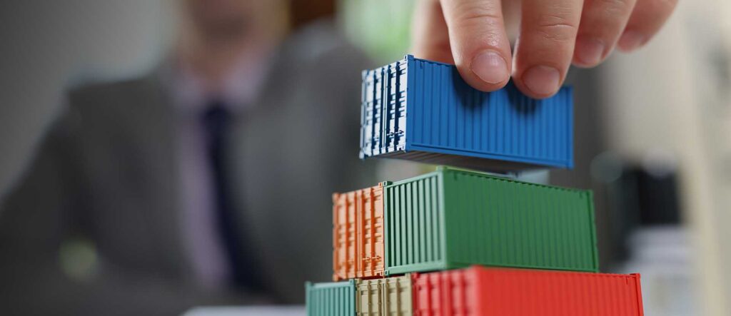 Business man arranging several cargo containers on his table with financial reports. Shipping, logistics and freight transportation concept.
